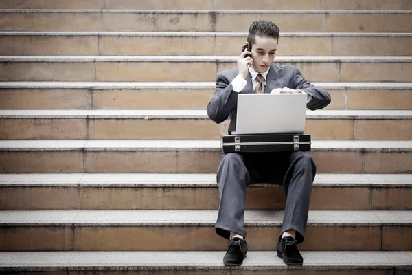 Hombre de negocios guapo que tiene llamada telefónica y el uso de ordenador portátil — Foto de Stock