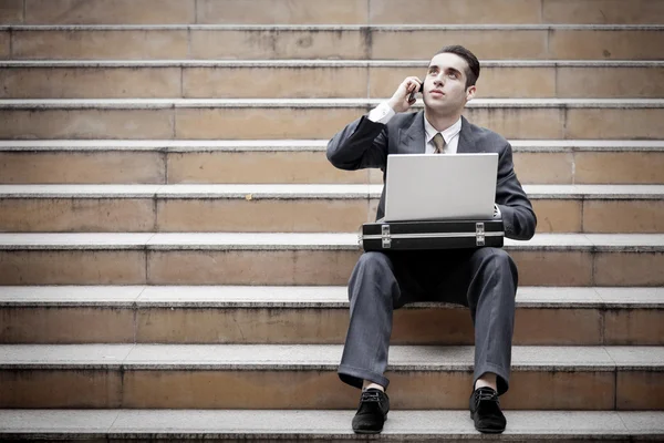 Hombre de negocios guapo que tiene llamada telefónica y el uso de ordenador portátil — Foto de Stock