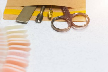 Tırnak makası, tırnak törpüsü, tırnak törpüsü ve makas; el işi zarfında bir takım tırnak cilası örnekleri, fotokopi alanı olan özel bir pedikür salonunda masanın üstünde duruyor.