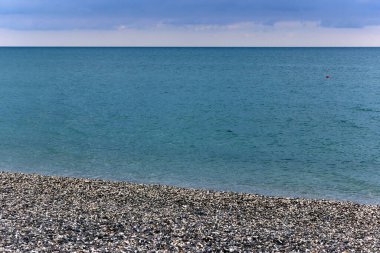 Akşamları sakin mavi deniz. Çakıl taşı plajından su yüzeyinin görüntüsü. Gökyüzündeki kara bulutlar. Doğal deniz manzarası.