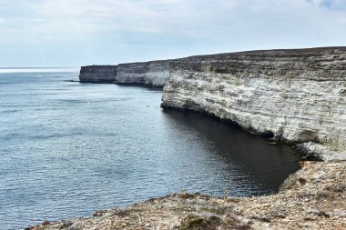 Deniz kenarında bir pelerin. Deniz manzarası, ufuk çizgisi, sakin deniz. Kötü hava, yaklaşan bulutlar, bulutların ardında batan güneş. Chalk rock, Cape Tarkhankut, Kırım. Beyaz taşın doğal dokusu. 