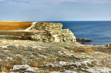 Chalk rock, Cape Tarkhankut, Kırım. Uçurumun kenarında bir köy yolu. Portakal diyarı, deniz kenarında bir pelerin. Deniz manzarası, ufuk, sakin mavi deniz, yükselen bulutlarla gökyüzü..