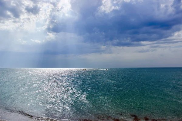 Bulutlu havada sakin mavi deniz. Yaz tatili. Güneş ışınları bulutların arasından denizi aydınlatır. Uzakta muz teknesine binen bir grup insan. Bir jet ski insanlarla muz teknesi çeker.. 
