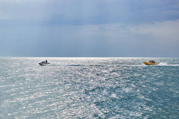 Bir jet ski insanlarla muz teknesi çeker. Muz teknesi gezisi. Bulutlu havada sakin mavi deniz. Eğlenceli bir yaz tatili.. 