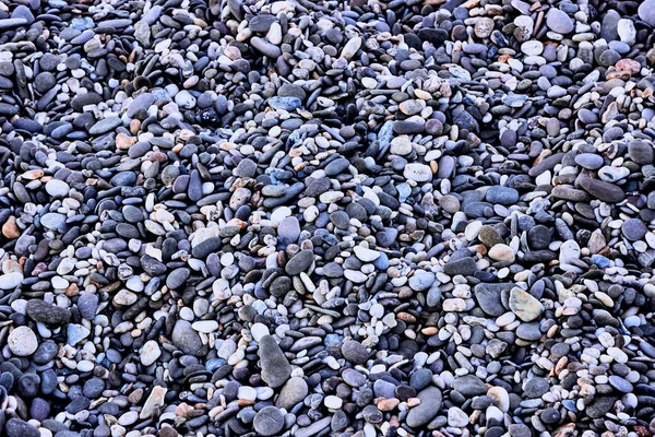 Background of small sea pebbles, top view. The texture of sea stones. Stones on the sea. Natural materials and colors of sea stones. Purple-blue shade. Horizontal photo.