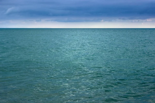 Akşamları küçük dalgalarla mavi deniz. Suyun yüzeyinde dalgalanmalar. Gökteki koyu mavi bulutlar. Doğal deniz manzarası.