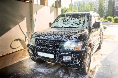 Otomobil yıkamada siyah bir SUV. Arabayı kendi ellerinle yıkıyorsun. Köpüklü siyah bir araba..