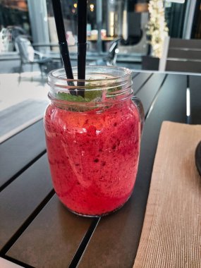 Bright pink berry cocktail, ice cream with mint and a straw in a transparent glass mug. Berry smoothie. Sweet pleasure. Cold refreshing dessert in the cafe.
