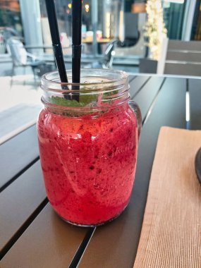 Bright pink berry cocktail, ice cream with mint and a straw in a transparent glass mug. Sweet pleasure. Berry smoothie. Cold refreshing dessert in the cafe.