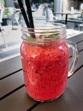 Bright pink berry cocktail, ice cream with mint and a straw in a transparent glass mug. Sweet pleasure. Cold refreshing dessert in the cafe. Berry smoothie. Side view.