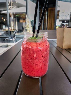 Berry smoothie. Cold refreshing dessert in the cafe. Bright pink berry cocktail, ice cream with mint and a straw in a transparent glass mug. Sweet pleasure. 