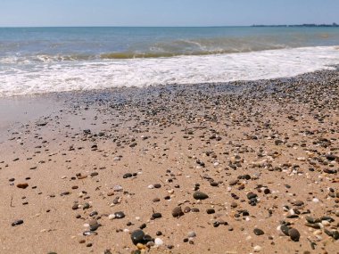 Sea pebbles, blue sea, waves, bright sun. Landscape wallpaper and nature concept. Warm summer sea with small waves in good weather.