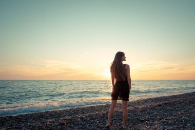Günbatımı arka planında ince bir kızın silueti. Güneş denizin ufkundan batıyor. İyi akşamlar, hafif bir esinti ve kıyıda genç bir bayan. Tüylerim diken diken oldu. - Rusya. İyi günler. Yaz.