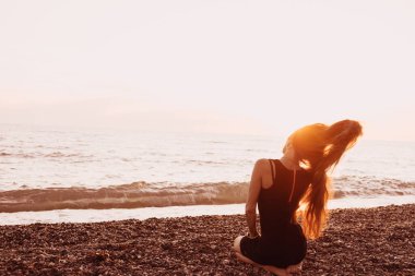 Günbatımı arka planında ince bir kızın silueti. Güneş denizin ufkundan batıyor. İyi akşamlar, hafif bir esinti ve kıyıda genç bir bayan. Tüylerim diken diken oldu. - Rusya. İyi günler. Yaz.