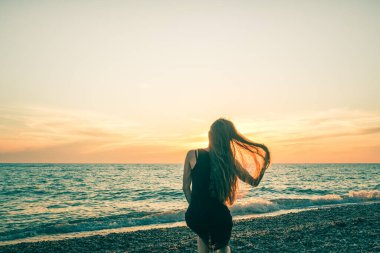 Günbatımı arka planında ince bir kızın silueti. Güneş denizin ufkundan batıyor. İyi akşamlar, hafif bir esinti ve kıyıda genç bir bayan. Tüylerim diken diken oldu. - Rusya. İyi günler. Yaz.