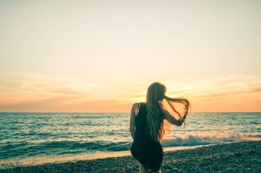 Günbatımı arka planında ince bir kızın silueti. Güneş denizin ufkundan batıyor. İyi akşamlar, hafif bir esinti ve kıyıda genç bir bayan. Tüylerim diken diken oldu. - Rusya. İyi günler. Yaz.