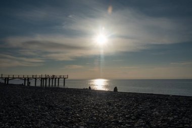 Denizin üzerinde gün batımı. İskeleden panorama. Çakıl taşı sahili. İnsanlar günü göremiyor. Karadeniz. Georgia.
