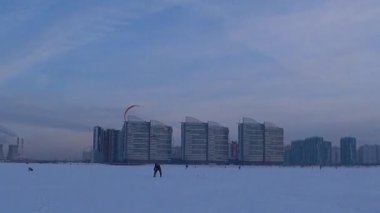 Mavi gökyüzüne karşı paraglider. İnsanlar soğuk bir kış gününde buzun üzerinde dinlenirler. Körfezde donmuş su. Deniz yüzeyinde buz ve kar. İnsanlar aktif olarak buz üzerinde dinleniyor ve paraşütle atlıyorlar. - Rusya. Kış. Gün.