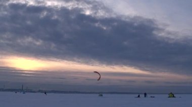 Mavi gökyüzüne karşı paraglider. İnsanlar soğuk bir kış gününde buzun üzerinde dinlenirler. Körfezde donmuş su. Deniz yüzeyinde buz ve kar. İnsanlar aktif olarak buz üzerinde dinleniyor ve paraşütle atlıyorlar. - Rusya. Kış. Gün.