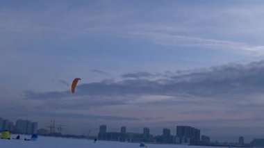Mavi gökyüzüne karşı paraglider. İnsanlar soğuk bir kış gününde buzun üzerinde dinlenirler. Körfezde donmuş su. Deniz yüzeyinde buz ve kar. İnsanlar aktif olarak buz üzerinde dinleniyor ve paraşütle atlıyorlar. - Rusya. Kış. Gün.