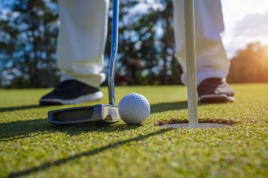 Golfçü topu yeşil golfün üstüne koyuyor, mercek akşam vakti parlıyor. Golfçü vuruşu uzun süre deliğe soktuktan sonra kazanır..                               