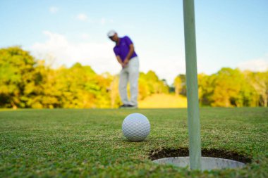 Golfçü topu yeşil golfün üstüne koyuyor, mercek akşam vakti parlıyor. Golfçü vuruşu uzun süre deliğe soktuktan sonra kazanır..                               