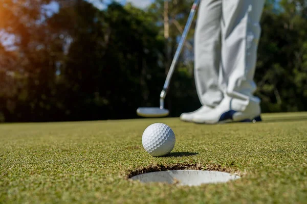 Golfçü topu yeşil golfün üstüne koyuyor, mercek akşam vakti parlıyor. Golfçü vuruşu uzun süre deliğe soktuktan sonra kazanır..                               