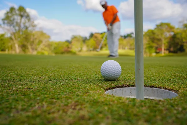 Golfçü topu yeşil golfün üstüne koyuyor, mercek akşam vakti parlıyor. Golfçü vuruşu uzun süre deliğe soktuktan sonra kazanır..                               