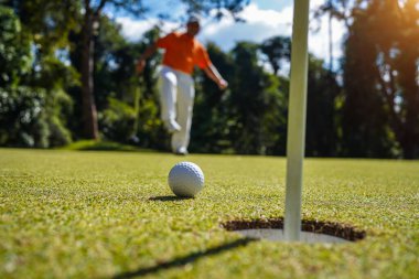 Golfçü topu yeşil golfün üstüne koyuyor, mercek akşam vakti parlıyor. Golfçü vuruşu uzun süre deliğe soktuktan sonra kazanır..                                