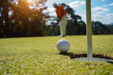 Golfçü topu yeşil golfün üstüne koyuyor, mercek akşam vakti parlıyor. Golfçü vuruşu uzun süre deliğe soktuktan sonra kazanır..                                