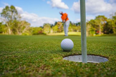 Golfçü topu yeşil golfün üstüne koyuyor, mercek akşam vakti parlıyor. Golfçü vuruşu uzun süre deliğe soktuktan sonra kazanır..                               