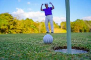 Golfçü topu yeşil golfün üstüne koyuyor, mercek akşam vakti parlıyor. Golfçü vuruşu uzun süre deliğe soktuktan sonra kazanır..                               