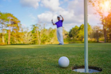 Golfçü topu yeşil golfün üstüne koyuyor, mercek akşam vakti parlıyor. Golfçü vuruşu uzun süre deliğe soktuktan sonra kazanır..                                