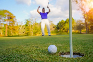 Golfçü topu yeşil golfün üstüne koyuyor, mercek akşam vakti parlıyor. Golfçü vuruşu uzun süre deliğe soktuktan sonra kazanır..                                