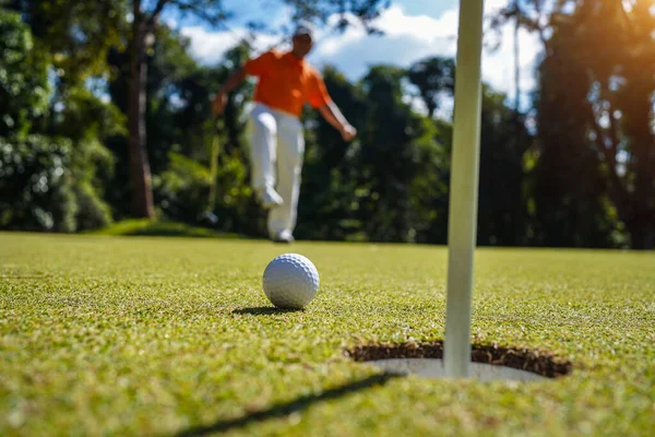 Golfçü topu yeşil golfün üstüne koyuyor, mercek akşam vakti parlıyor. Golfçü vuruşu uzun süre deliğe soktuktan sonra kazanır..                                