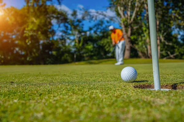 Golfçü topu yeşil golfün üstüne koyuyor, mercek akşam vakti parlıyor. Golfçü vuruşu uzun süre deliğe soktuktan sonra kazanır..                                