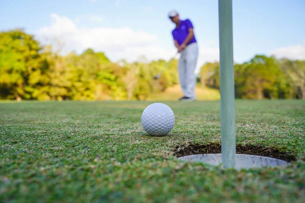 Golfçü topu yeşil golfün üstüne koyuyor, mercek akşam vakti parlıyor. Golfçü vuruşu uzun süre deliğe soktuktan sonra kazanır..                               