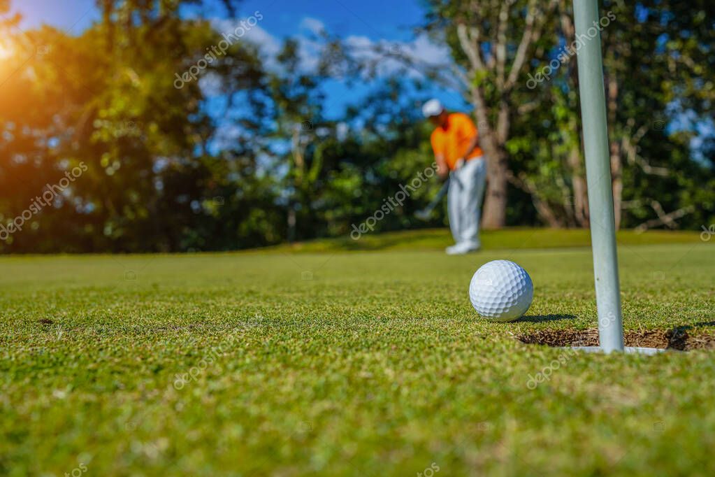 Golfer putting ball on the green golf, lens flare on sun set evening time. Golfer action to win after long putting golf ball in to the hole.