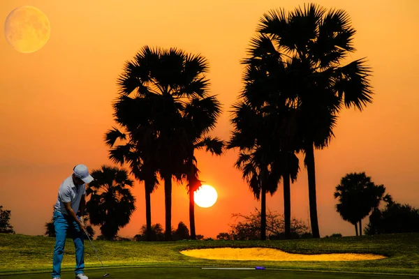 Golf player putting golf ball to hole during sunset or sunrise. View of Golf Course with beautiful green field. Golf course with a rich green turf beautiful scenery. Sport concept