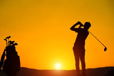 Golfçülerin golf topu gün batımındaki deliğe doğru siluetlendi. Kışın altın sabah gökyüzü, sisli yüksek dağ arkaplanı.                               