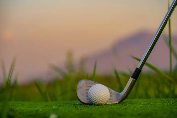 Golf club and ball on green grass ready to be struck on golf course background, Lens flare on sun set evening time. Golf ball on tee in front of driver on a golf course.