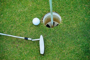 Yeşil sahada golf sopası olan bir golf topunun en üst görüntüsü. Golf topu ve golf sopası akşam golf sahasında güneş ışığı altında..                                 