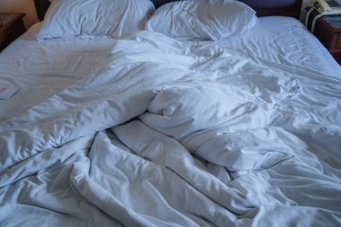 Beyaz yastıklı dağınık bir yatak ve yatağın üzerinde battaniye. Yapılmamış yatağın üzerinde beyaz battaniyeli birkaç yastık. Sabahları dinlenme zamanı kavramı. Rahatlama arkaplanı.