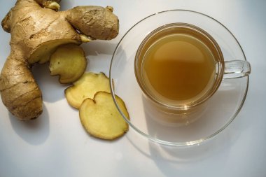 Sıcak zencefil suyu ve zencefil dilimleri sabah güneşinin altında beyaz bir masada, sıcak zencefil suyu vücut ısısını arttırır..                               