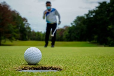 Golfçü topu yeşil golfün üstüne koyuyor, mercek akşam vakti parlıyor. Golfçü vuruşu uzun süre deliğe soktuktan sonra kazanır..                               