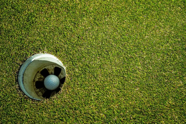 朝の日差しと美しいゴルフコースで緑の芝生の上に穴の中にゴルフボール ゴルフ場の緑の芝生の上のゴルフボール背景 — ストック写真