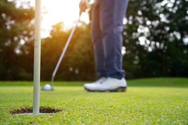 Golfçü topu yeşil golfün üstüne koyuyor, mercek akşam vakti parlıyor. Bulanık golfçü akşam golf sahasında güneş ışığıyla golf oynuyor.. 