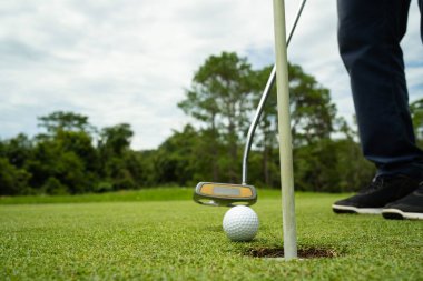 Golfçü topu yeşil golfün üstüne koyuyor, mercek akşam vakti parlıyor. Golf topları gün batımında golf sahasında golf oyuncuları tarafından delik deşik edilecek..