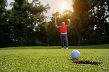 Golfçü topu yeşil golfün üstüne koyuyor, mercek akşam vakti parlıyor. Golf topları gün batımında golf sahasında golf oyuncuları tarafından delik deşik edilecek..