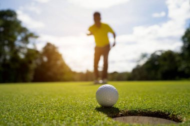 Golfçü topu yeşil golfün üstüne koyuyor, mercek akşam vakti parlıyor. Bulanık golfçü akşam golf sahasında güneş ışığıyla golf oynuyor.. 